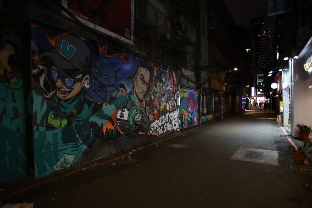 Explore the vibrant street art on display in a bustling urban alley at night.