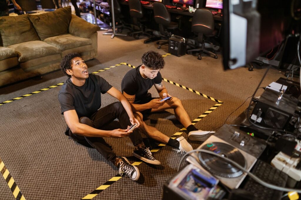 Two friends sitting on the floor playing video games indoors with controllers and enjoying the leisure time.