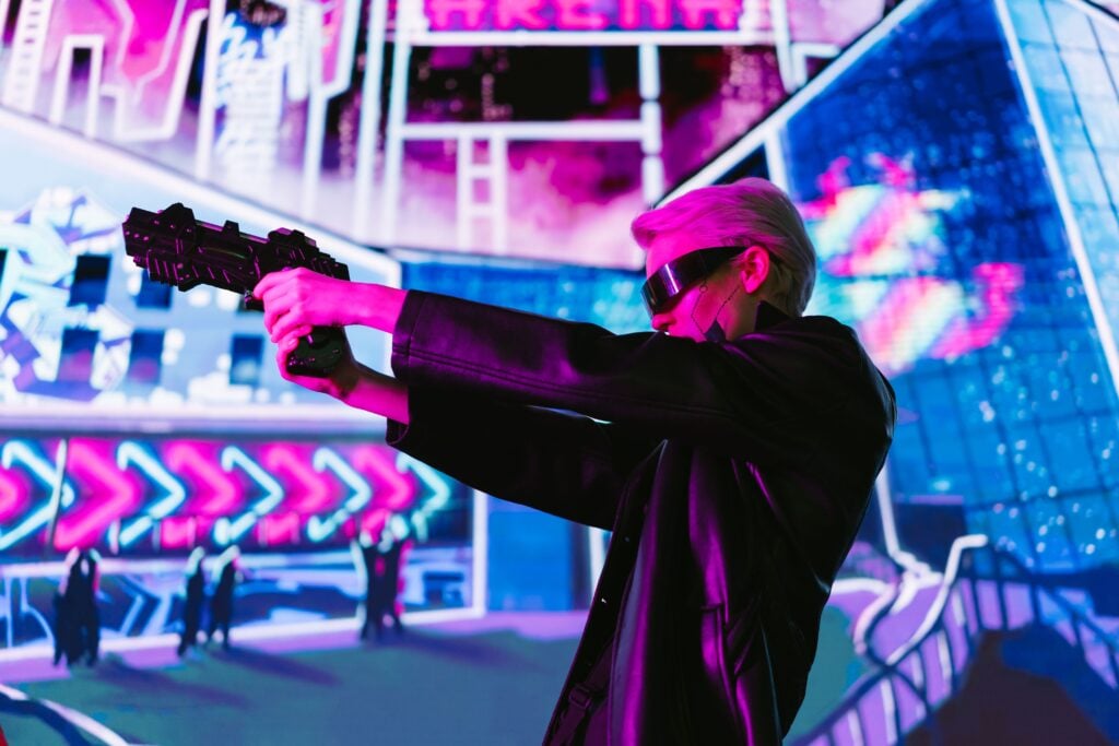 Person in cyberpunk attire aims futuristic gun in neon-lit scene