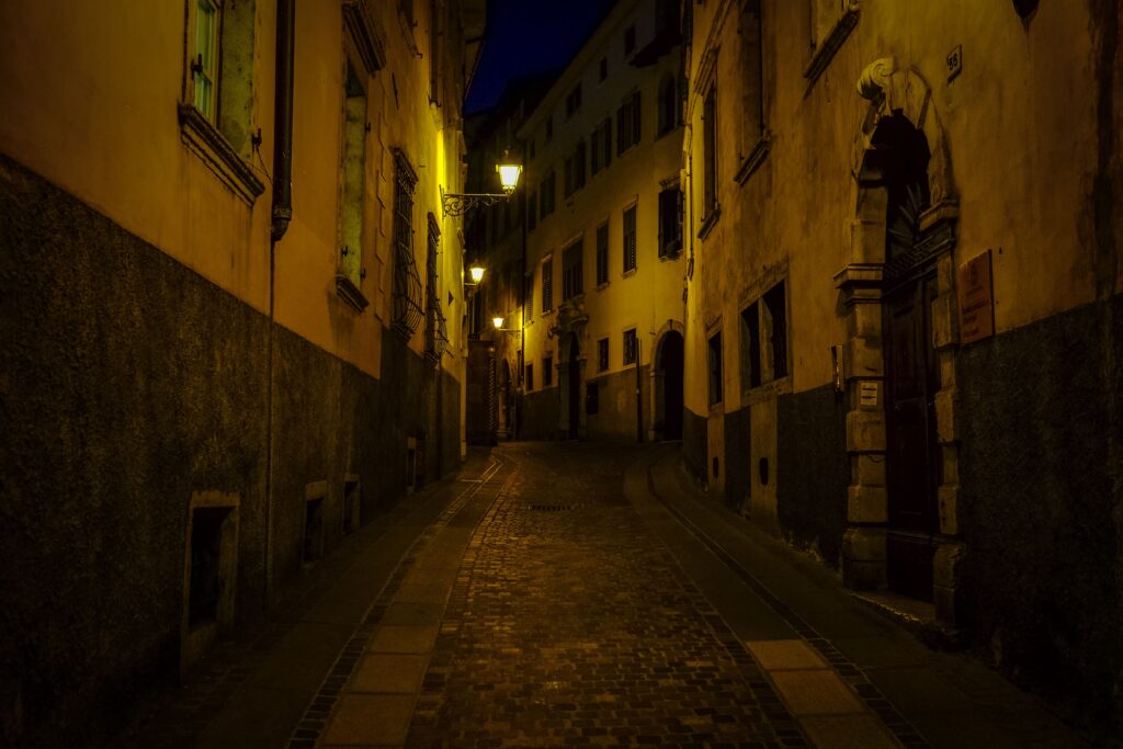 A dimly lit, narrow street in historic Rovereto, Italy, during the night, showcasing old world architecture.