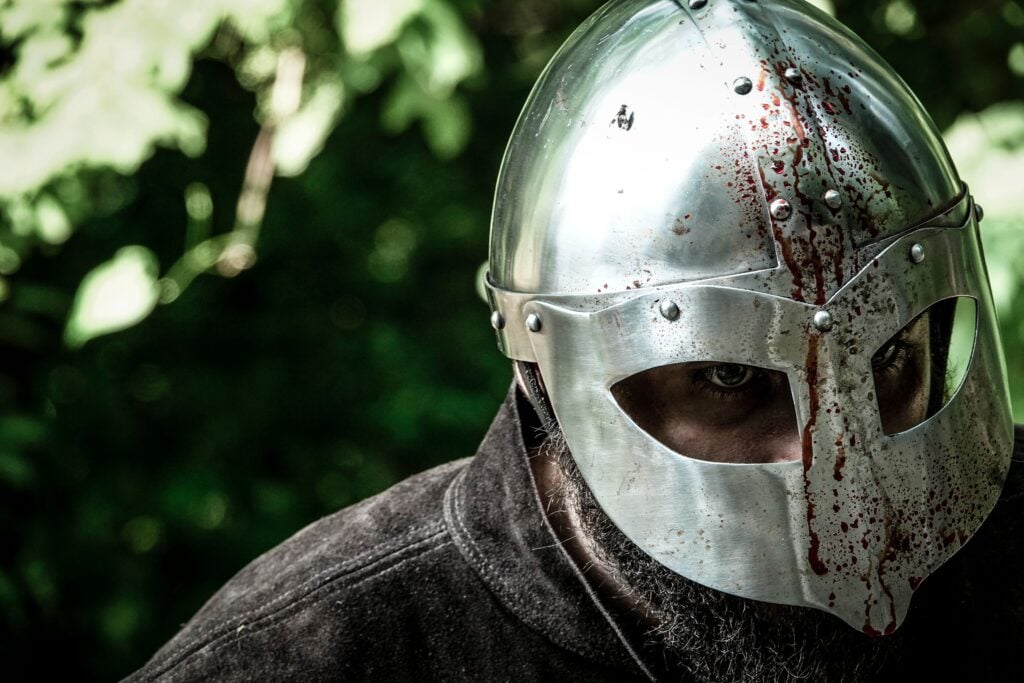 Close-up of a knight in a blood-stained helmet, evoking medieval combat.